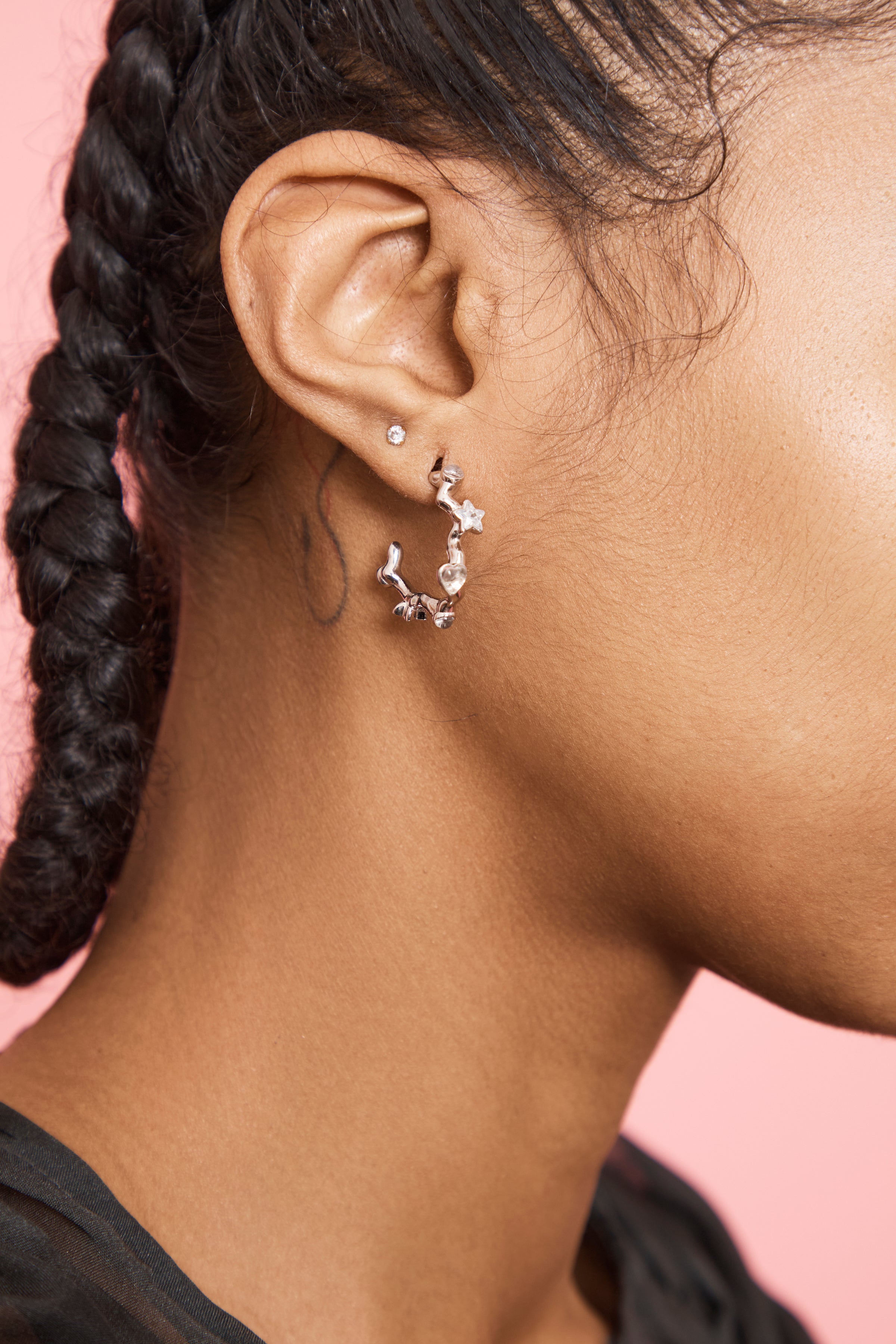 Close-up of person wearing a silver chunky hoop-style earring with a pink background