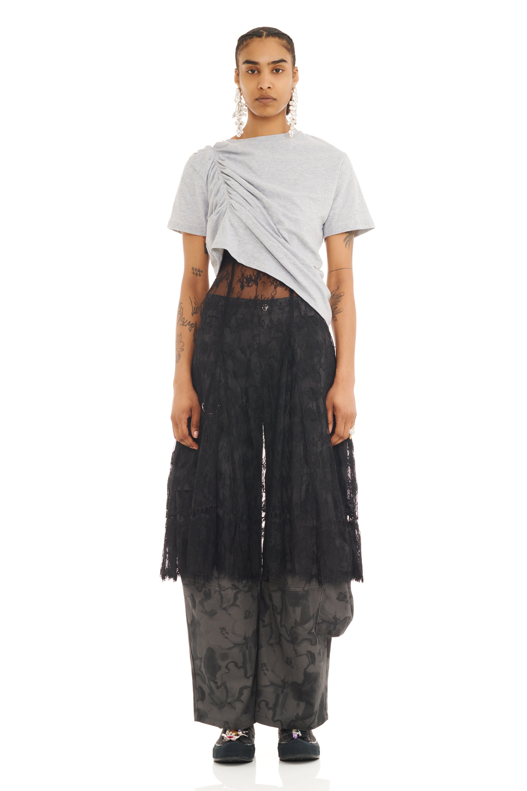 Person wearing a gray ruched tee with asymmetrical hem and black layered skirt over pants on a white background