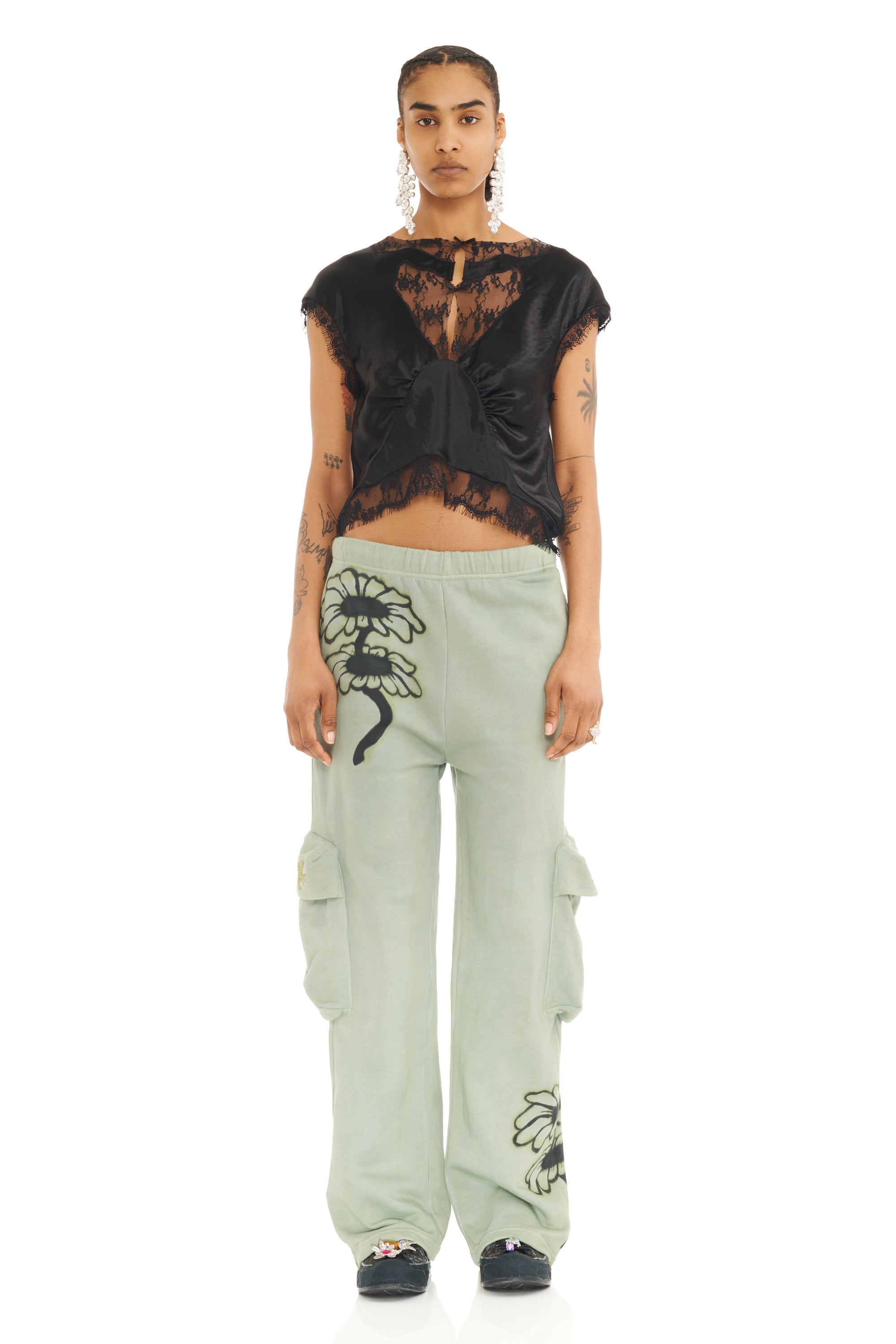 Person wearing a black lace top and light green pants with floral designs on a white background