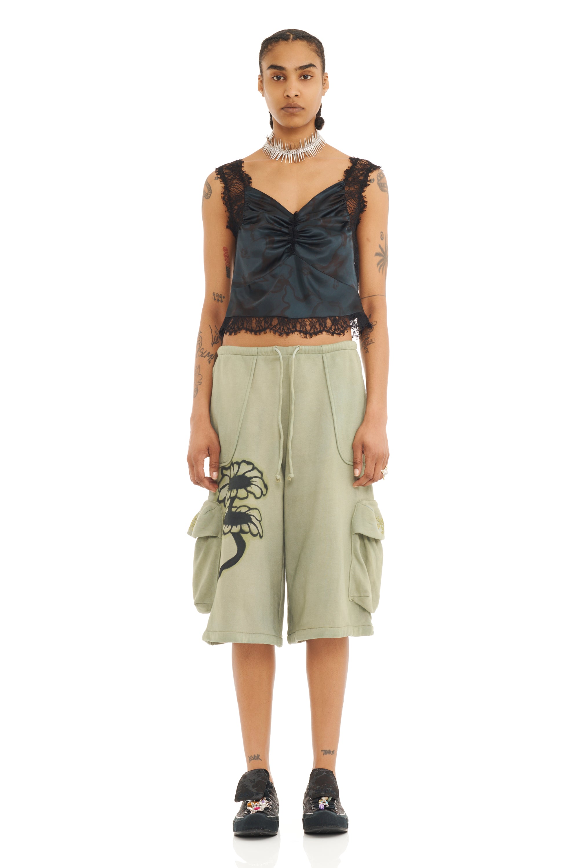 Woman wearing a black lace top with light green oversized baggy sweatshorts with a floral design and large cargo pockets.