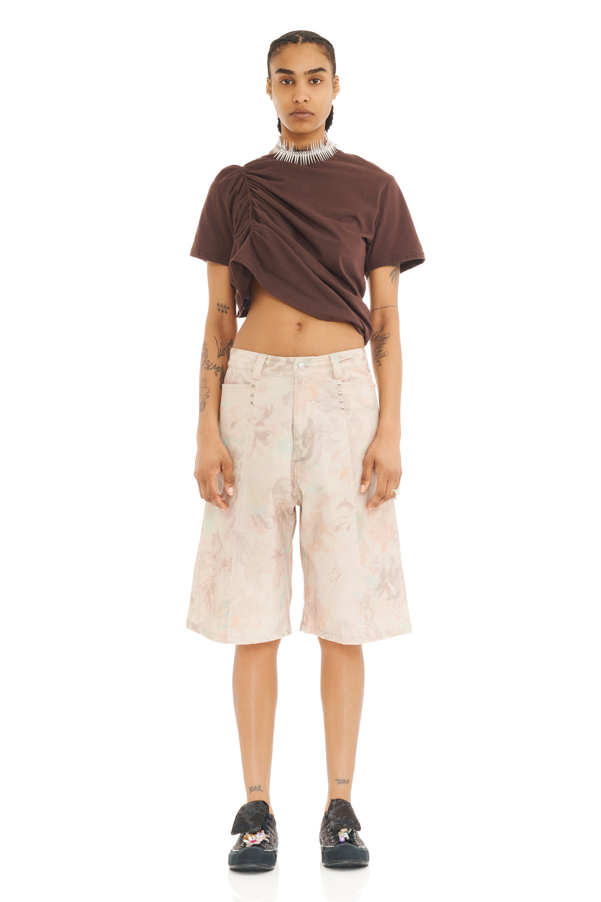 Person wearing a brown top and light-colored long shorts on a white background