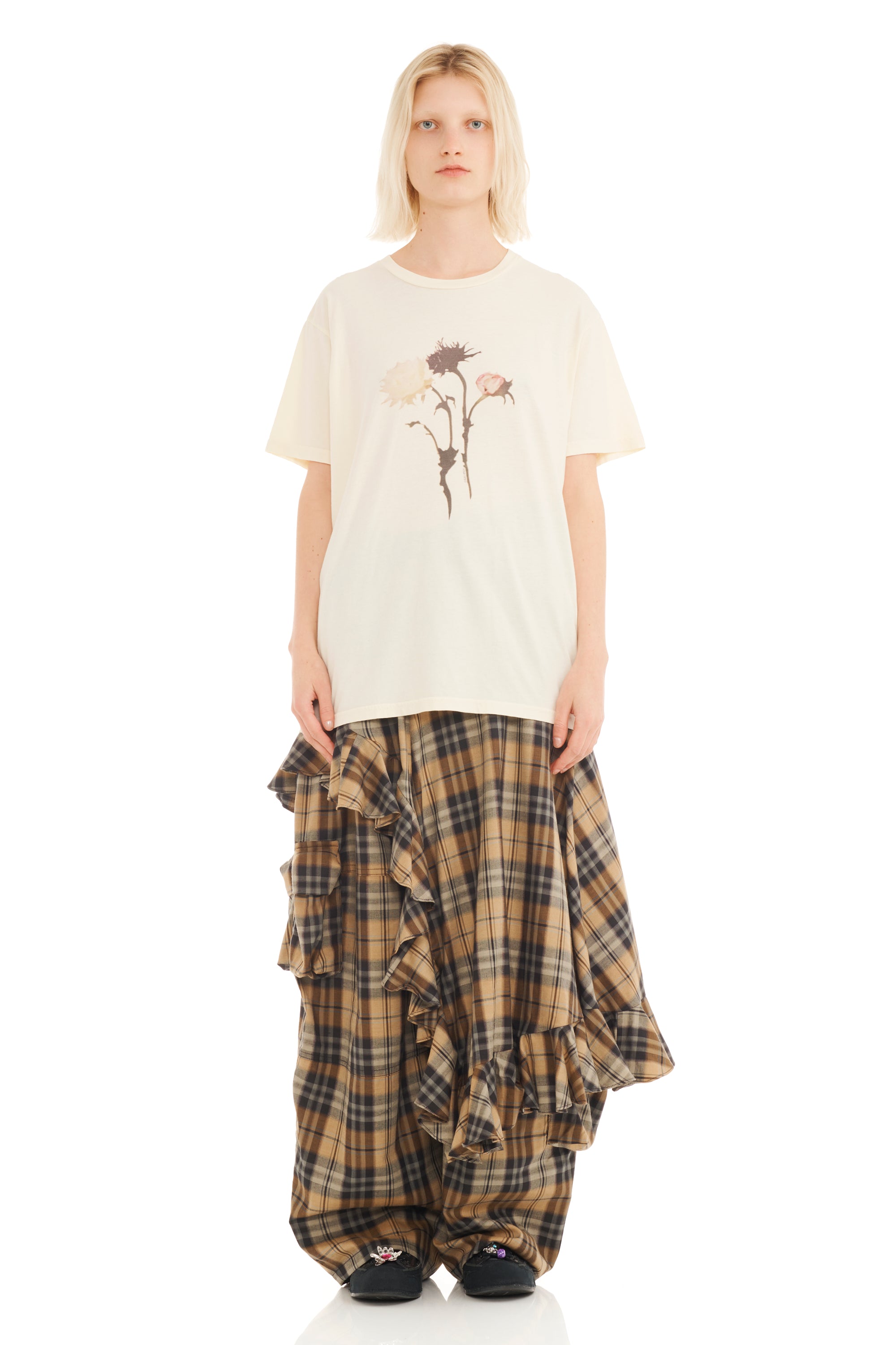 Person wearing a white t-shirt with a floral design and plaid skirt on a white background