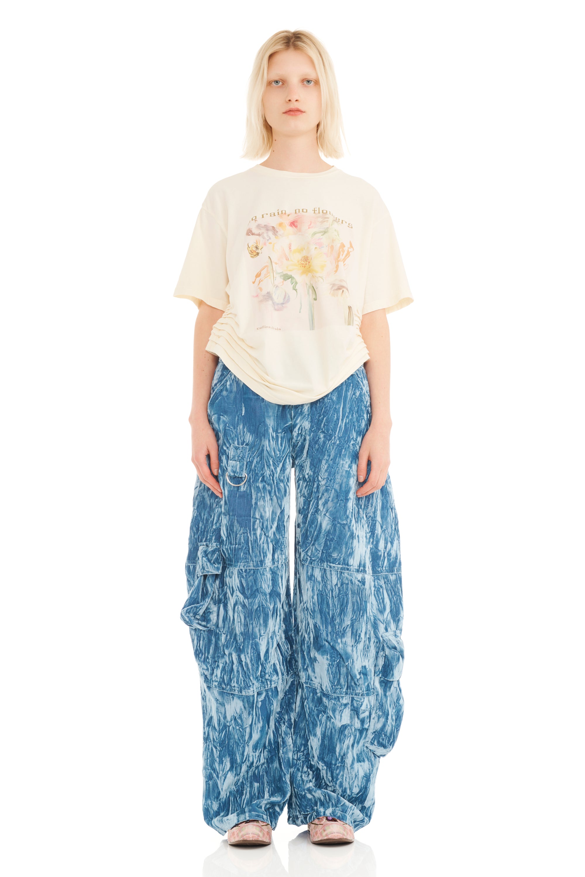 Person wearing a cream floral graphic t-shirt and blue patterned pants on a white background