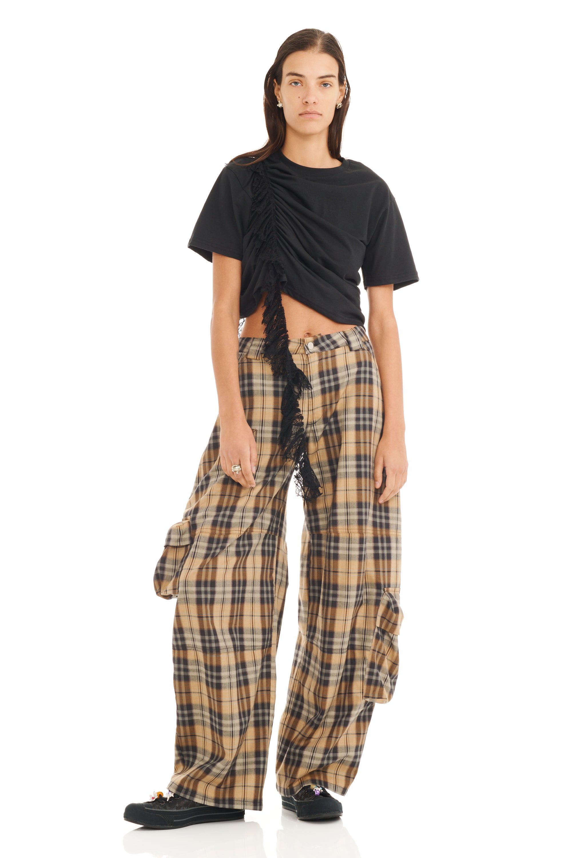 Person wearing a black ruched cropped top with trailing lace detail and plaid pants on a white background