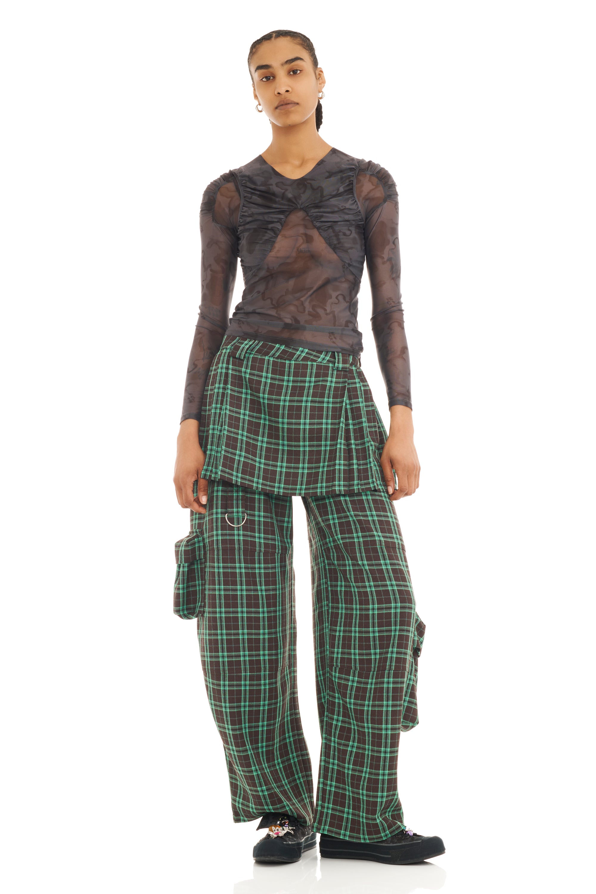 Person wearing a sheer black mesh long-sleeved top and plaid pants on a white background