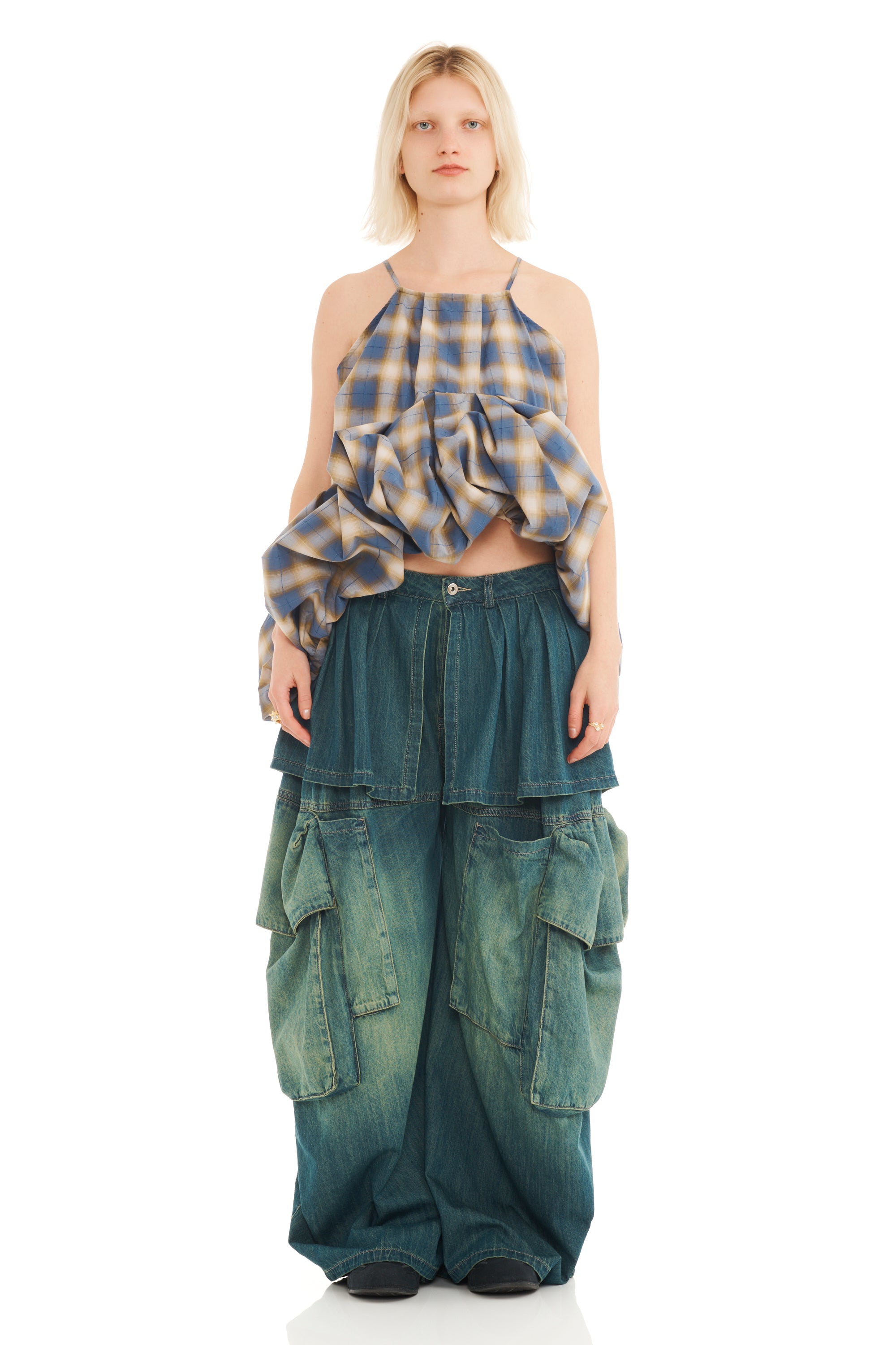 Woman wearing a plaid halter top with exaggerated ruffled hem and layered denim pants on a white background