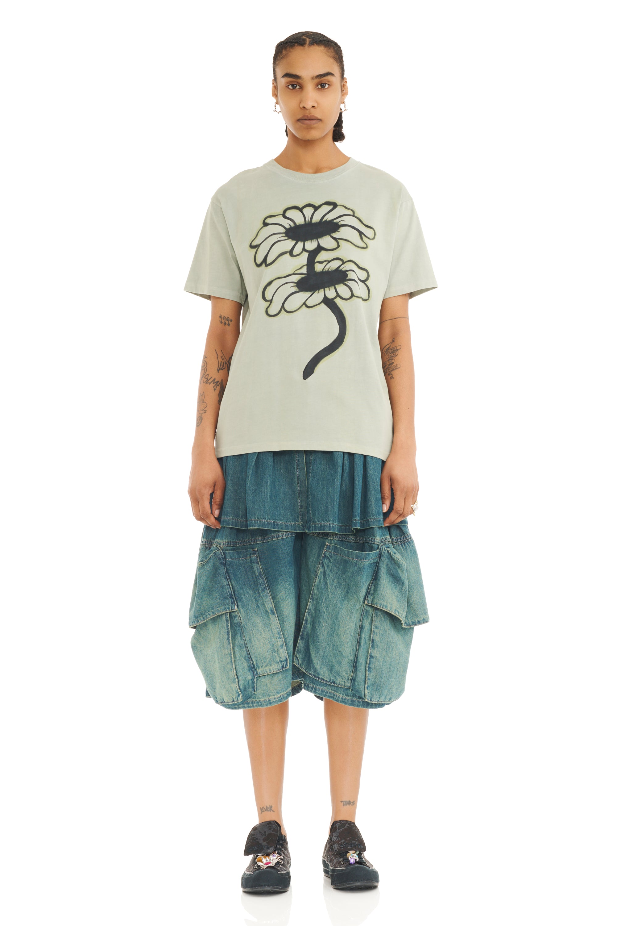 Person wearing a light olive t-shirt with a floral design and denim shorts on a white background