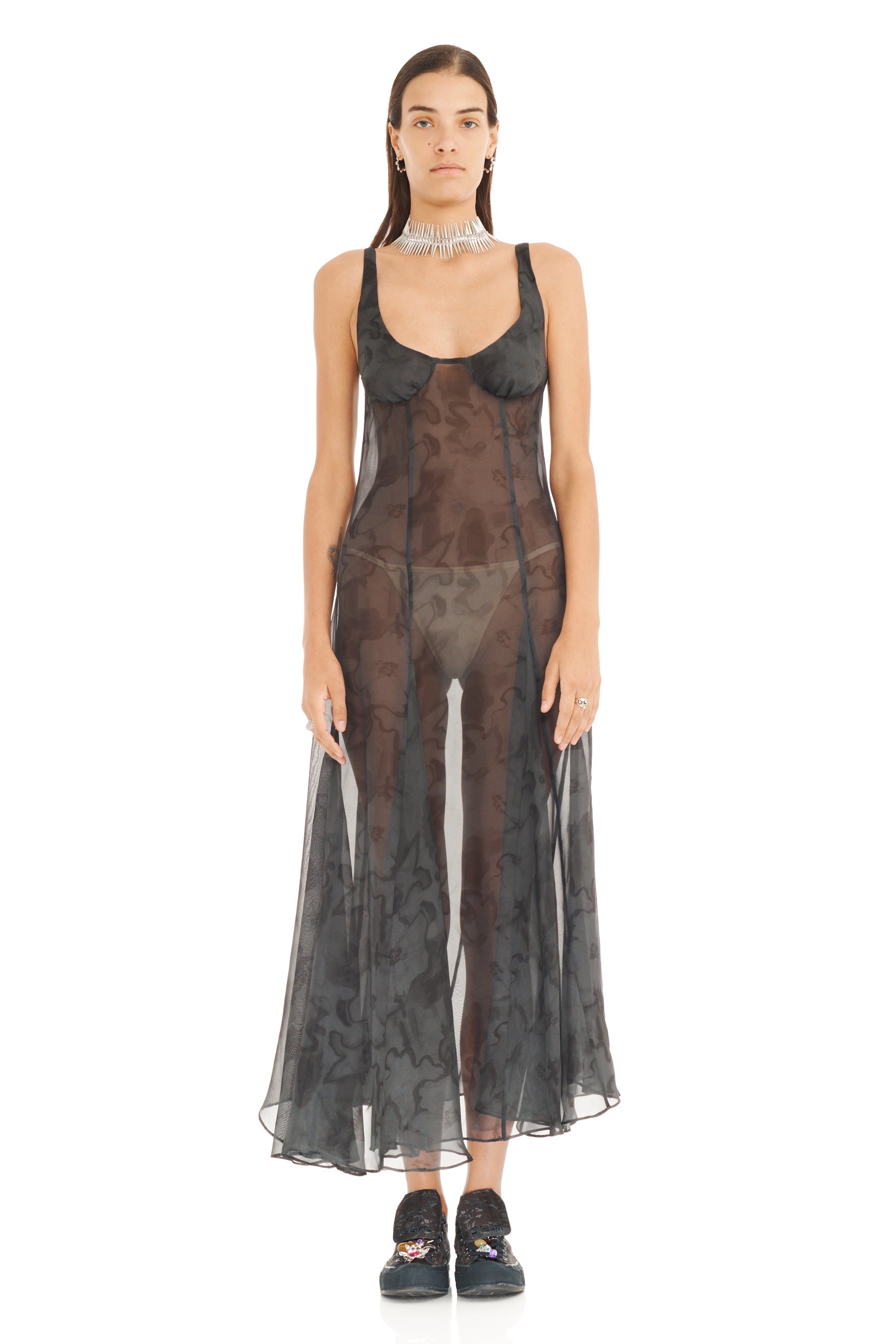 Model wearing a sheer black dress with floral patterns on a white background