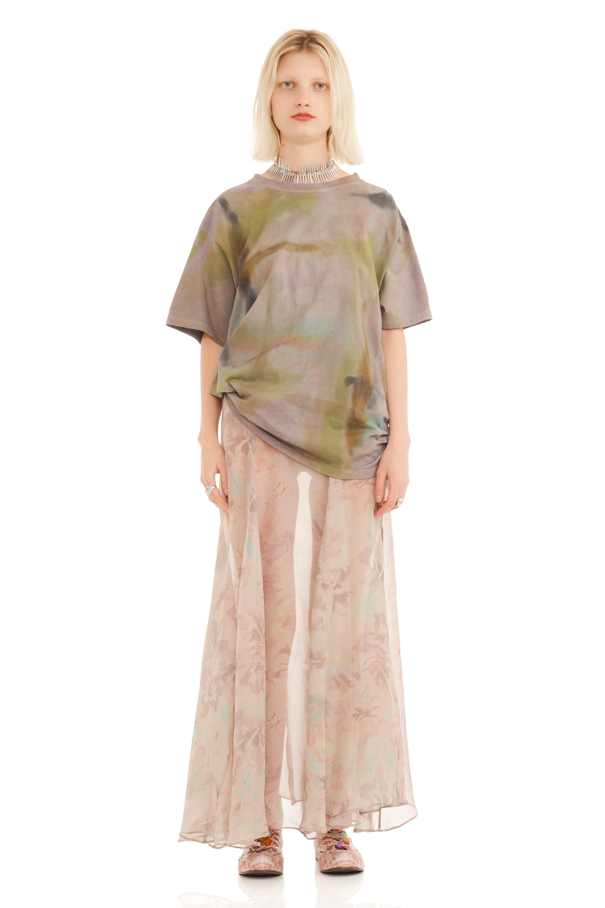 Woman wearing a green and beige tie dyed tee with side ruching atop a sheer beige skirt on a white background