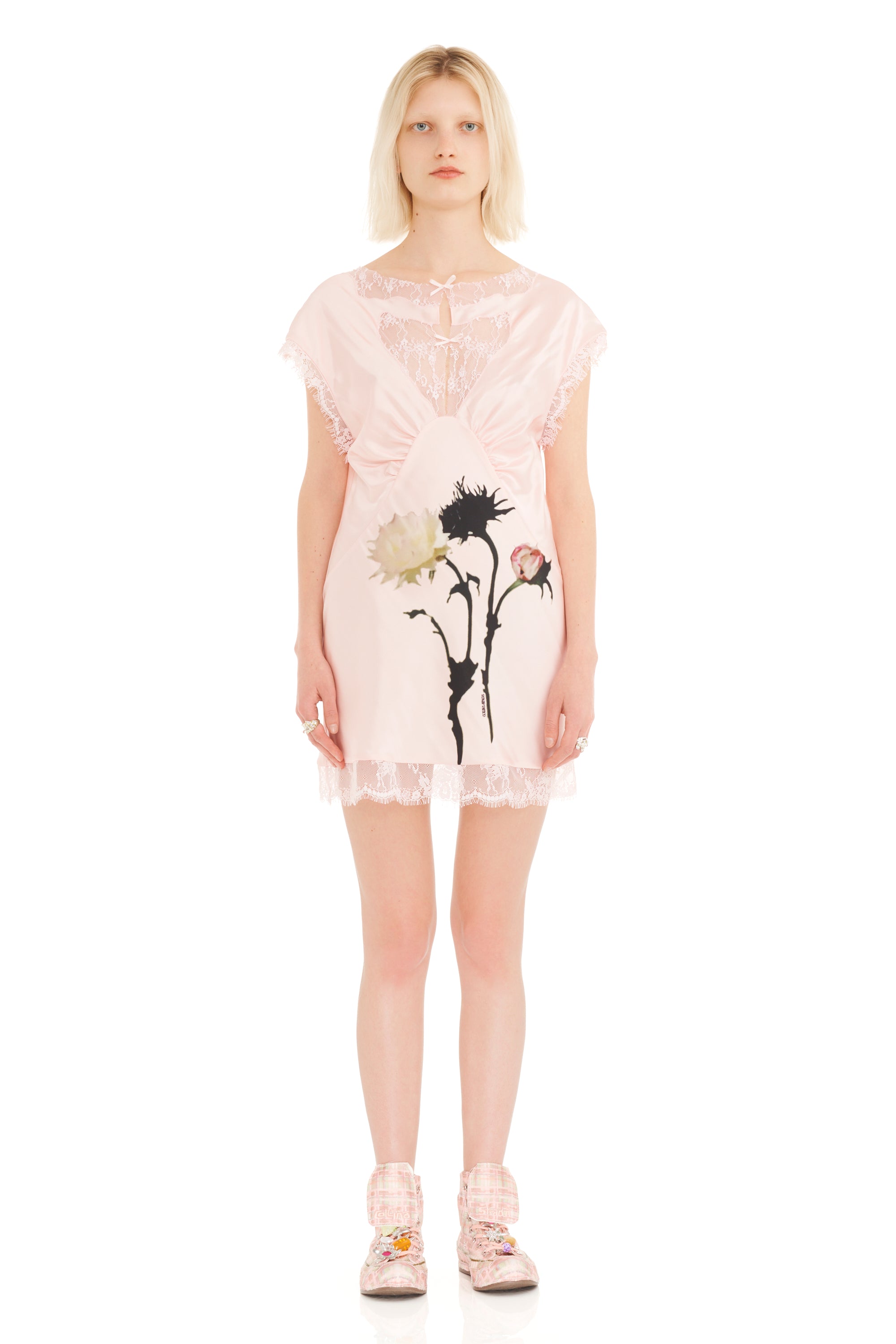 Woman wearing a blush pink lace dress with floral design and lace details on a white background