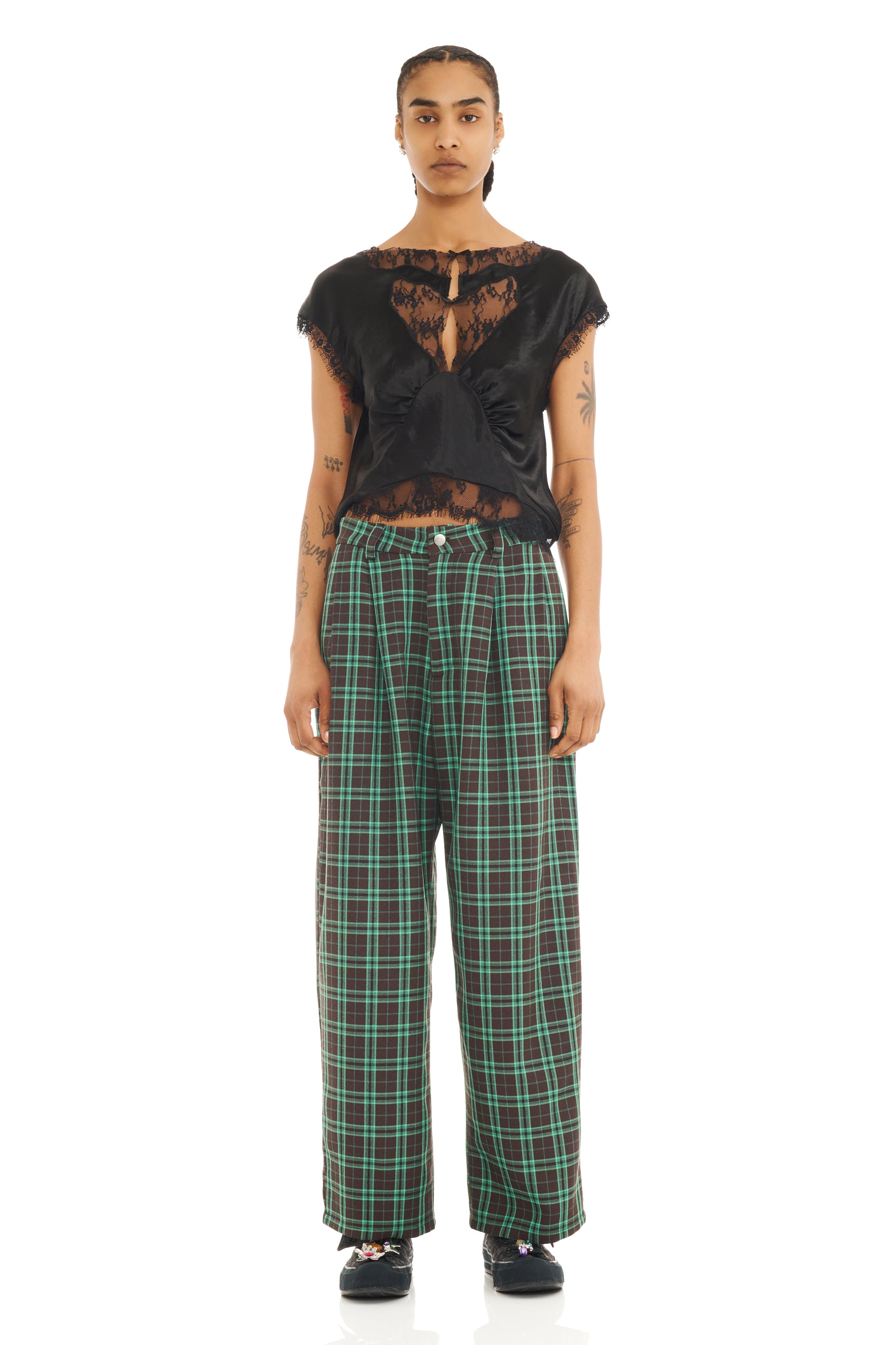 Person wearing a black lace top and plaid pants on a white background