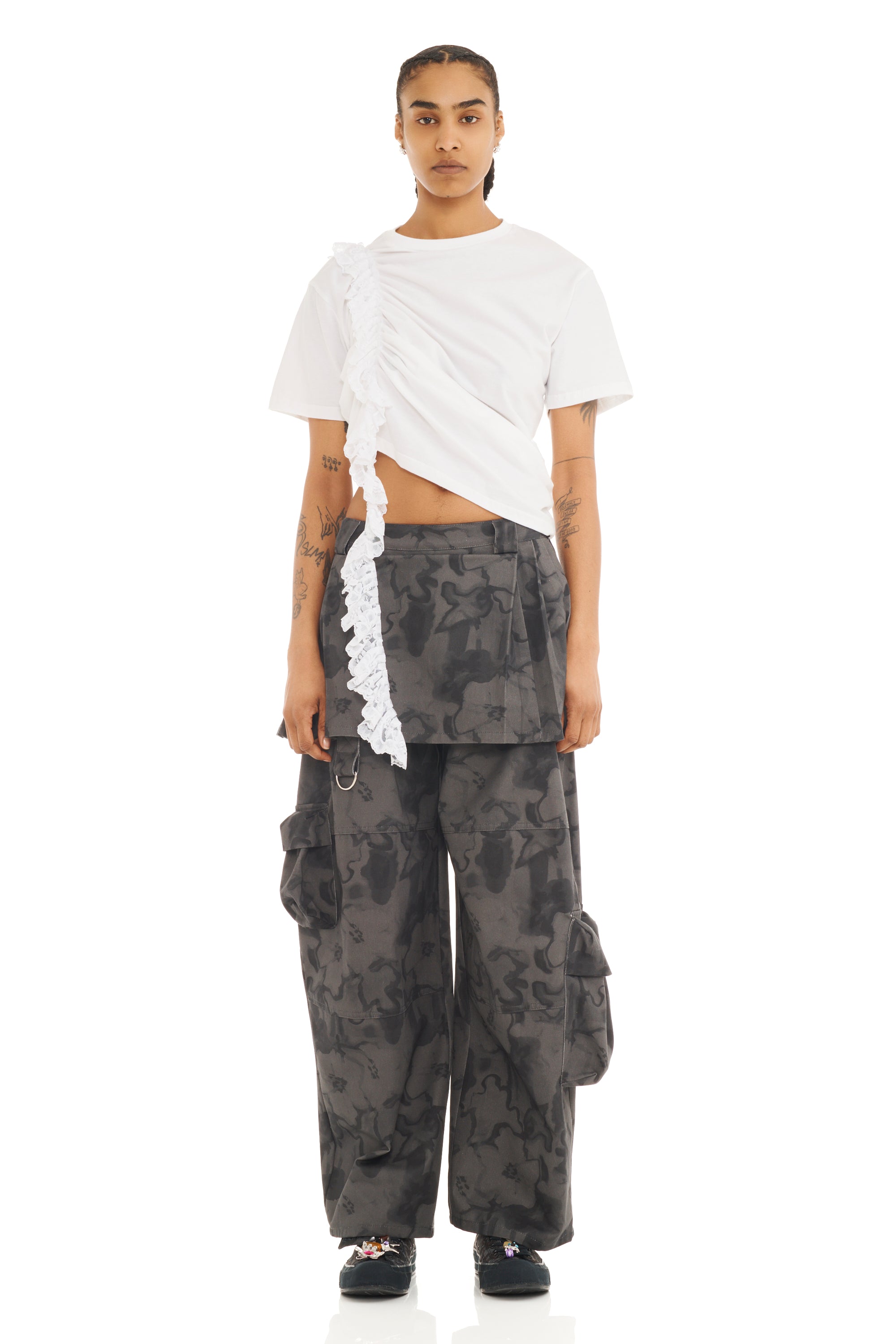 Person wearing a white ruched tee with trailing lace detail and camouflage pants on a white background