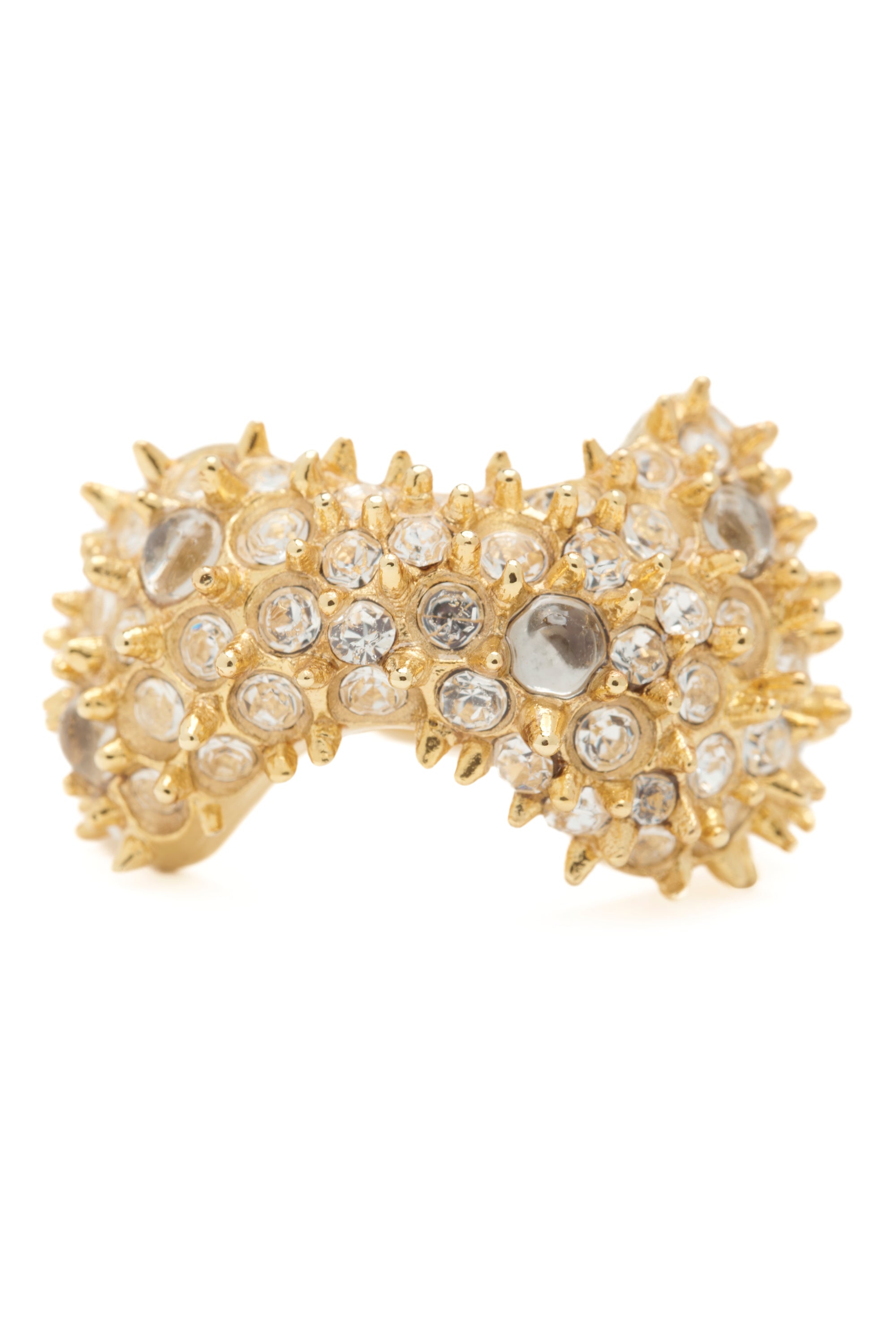 Gold bow-shaped ring with embedded crystals and mini spikes on a white background