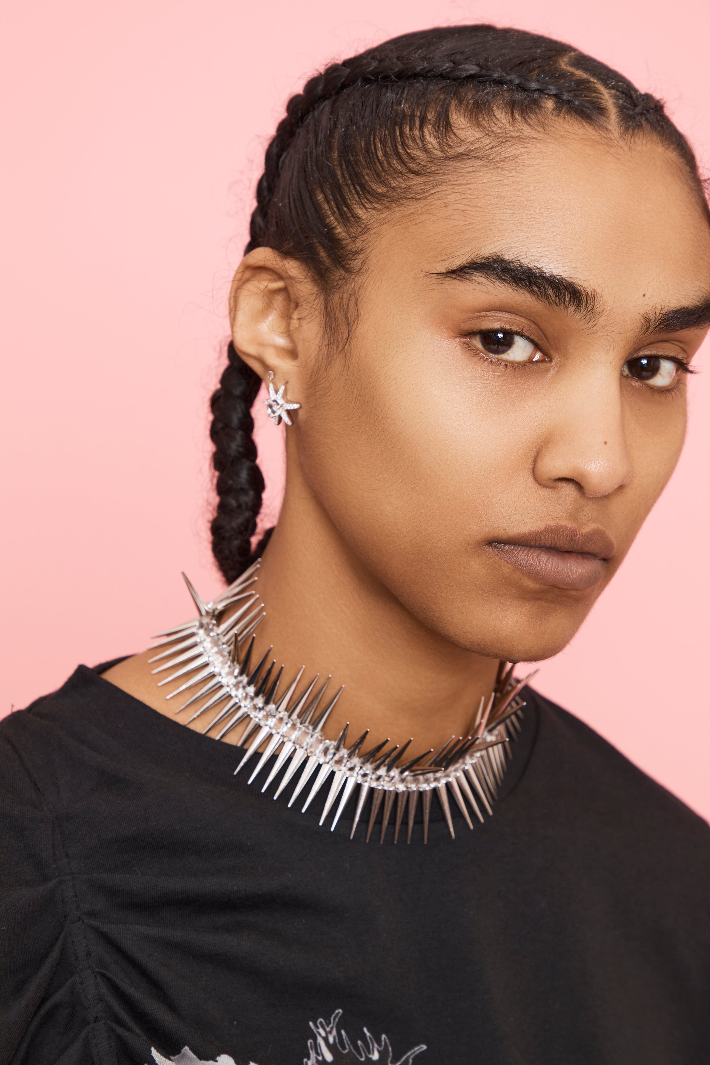 Person wearing star shaped silver earrings and a spikey necklace with a pink background