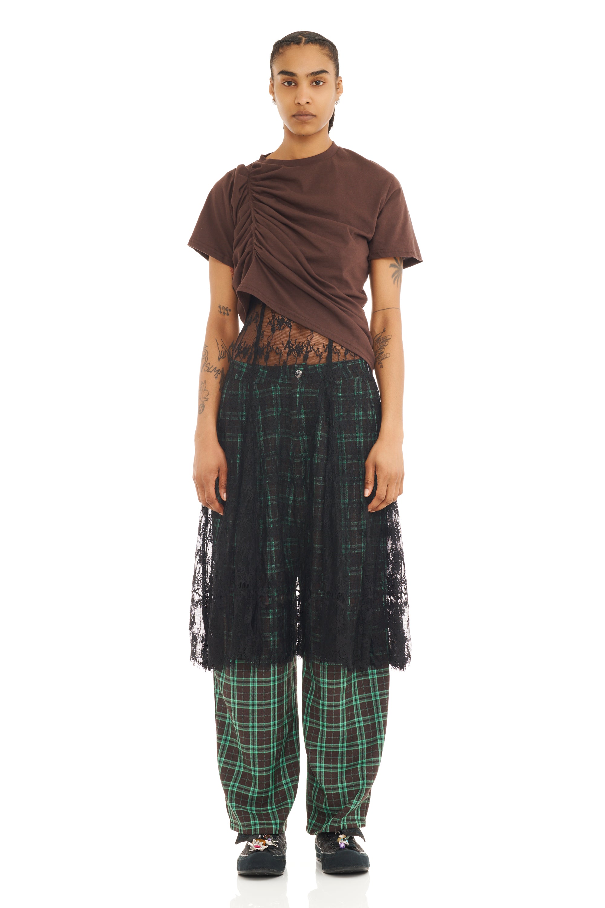 Person wearing a brown ruched top with asymmetrical hem and black lace skirt layered over checkered pants on a white background
