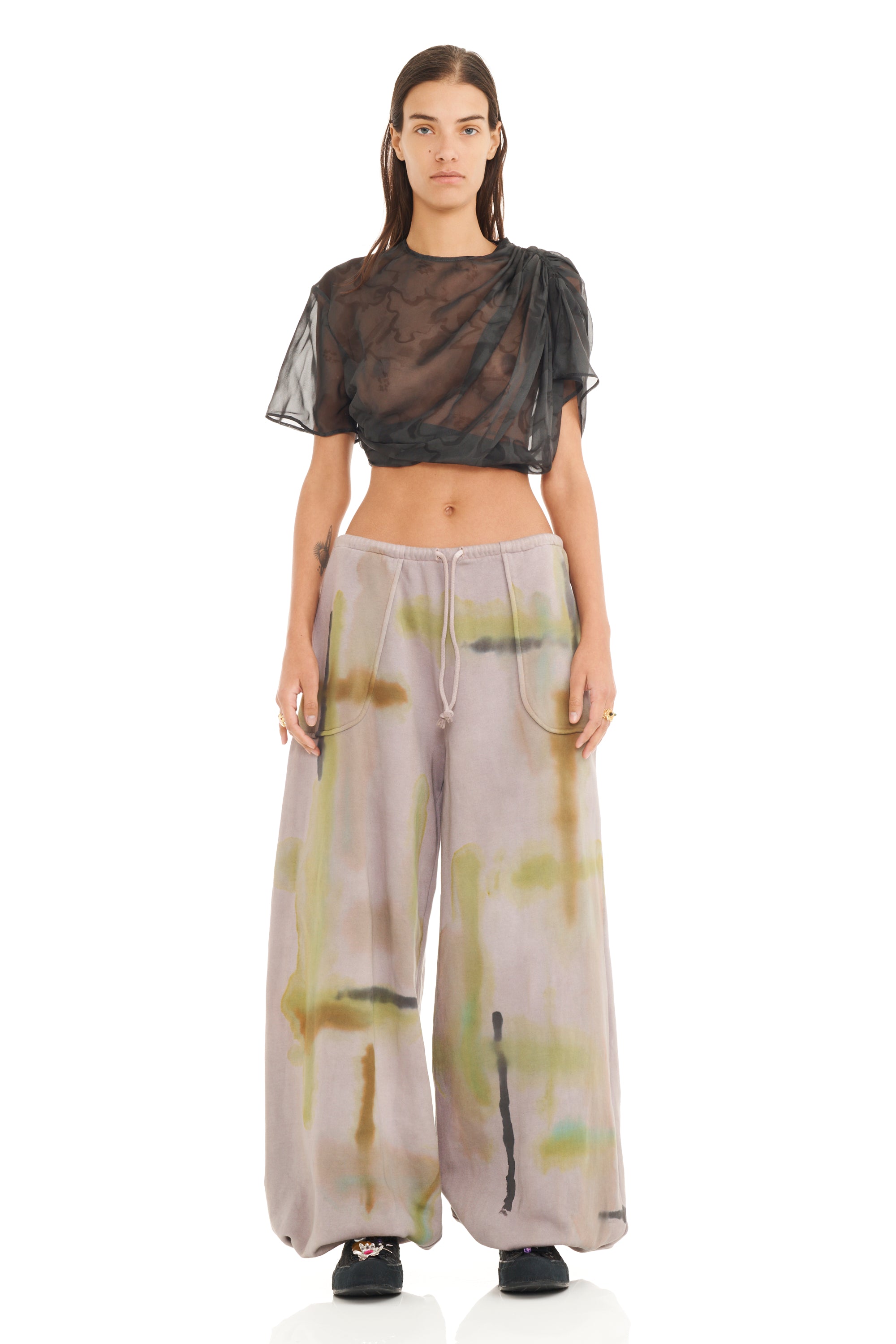 Model wearing a sheer black top and wide-leg sweatpants with abstract patterns on a white background