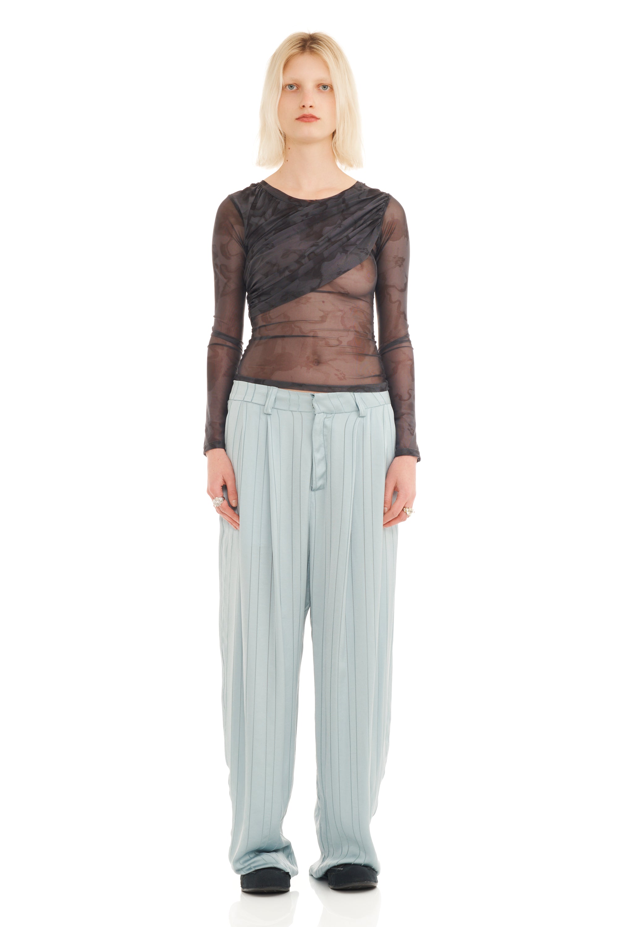 Woman wearing a sheer black top and light cerulean blue pants on a white background