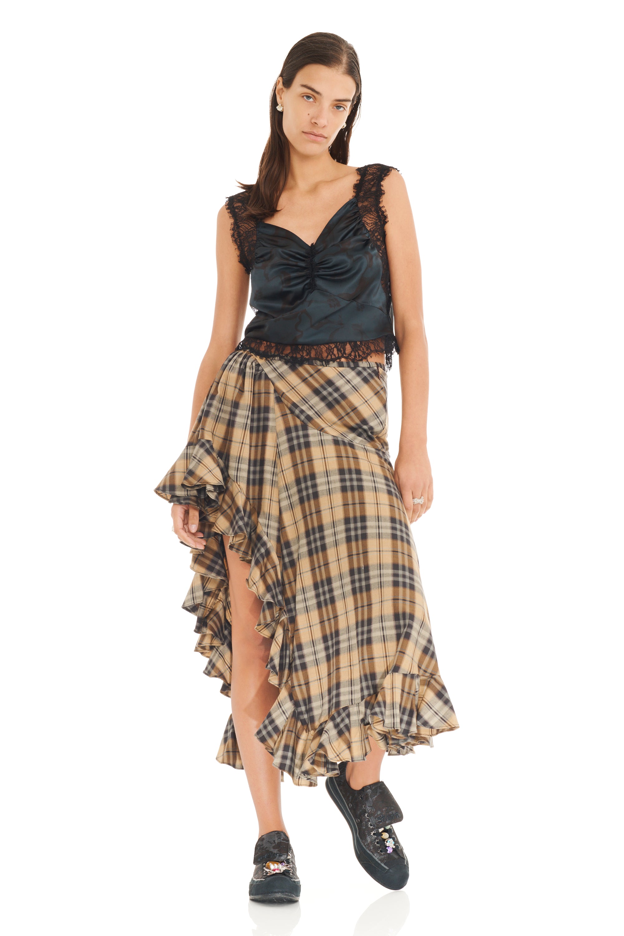Woman wearing a black lace tank top with ruched satin body and plaid skirt on a white background