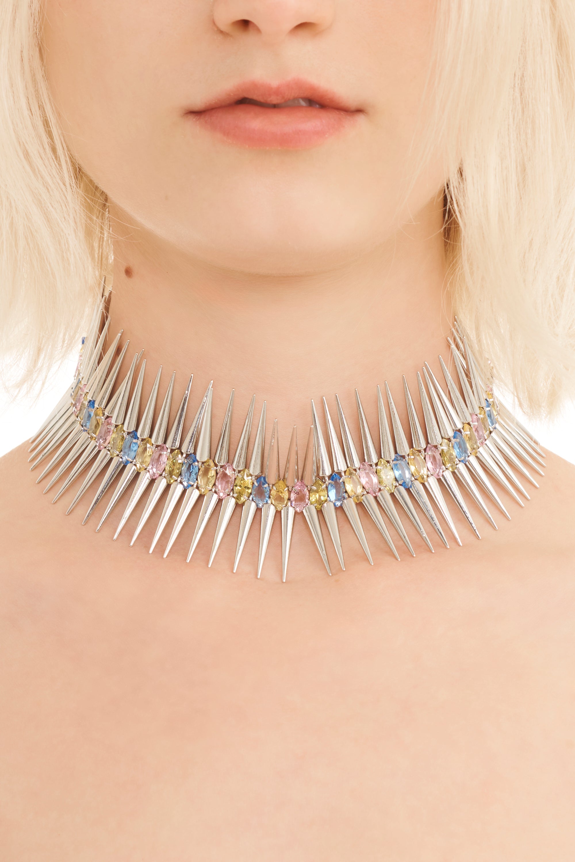 Necklace with spikes and multicolored stones worn by a person with blonde hair.