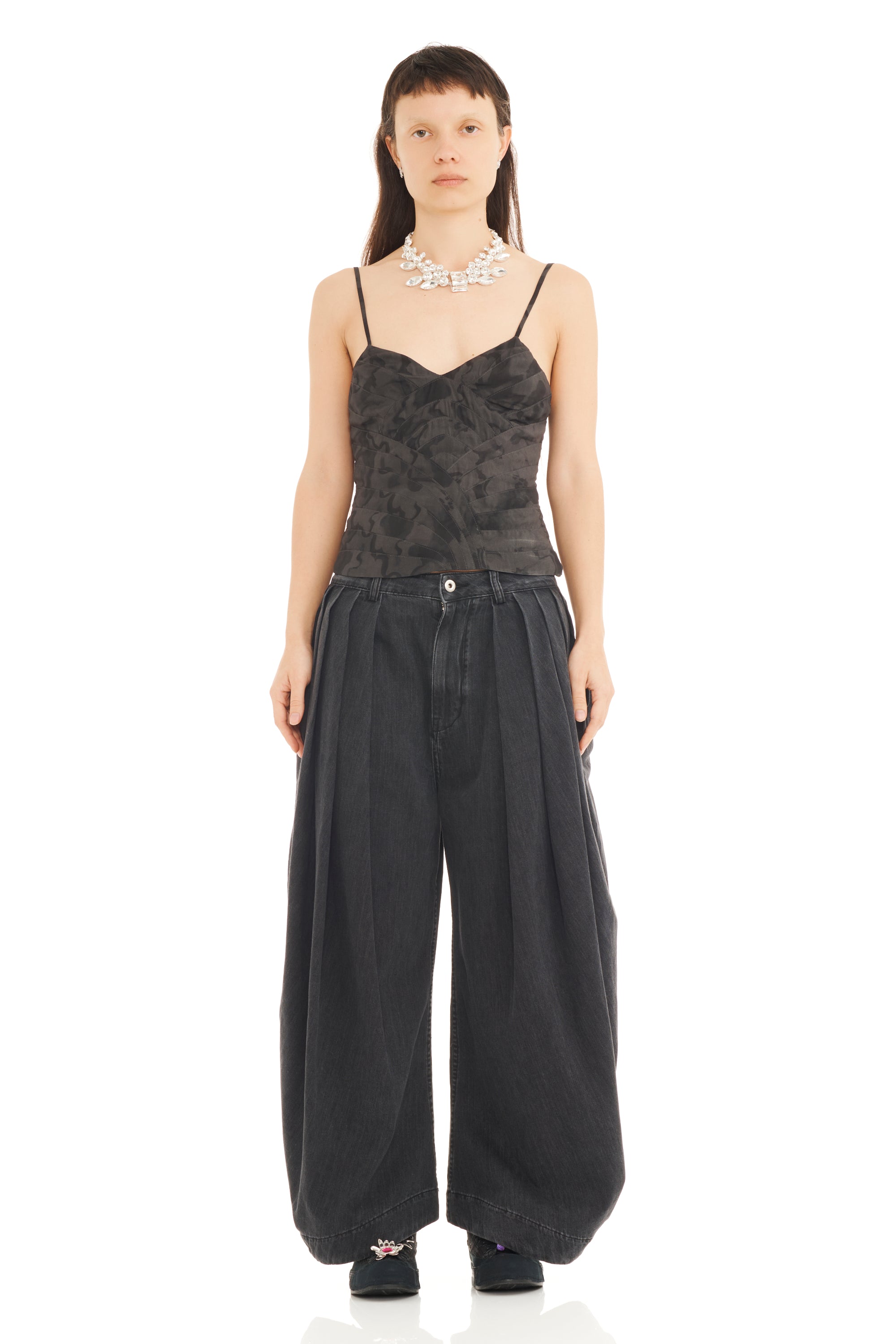 Woman wearing a camo tank camisole on top of charcoal grey baggy pleated trousers on a white background.