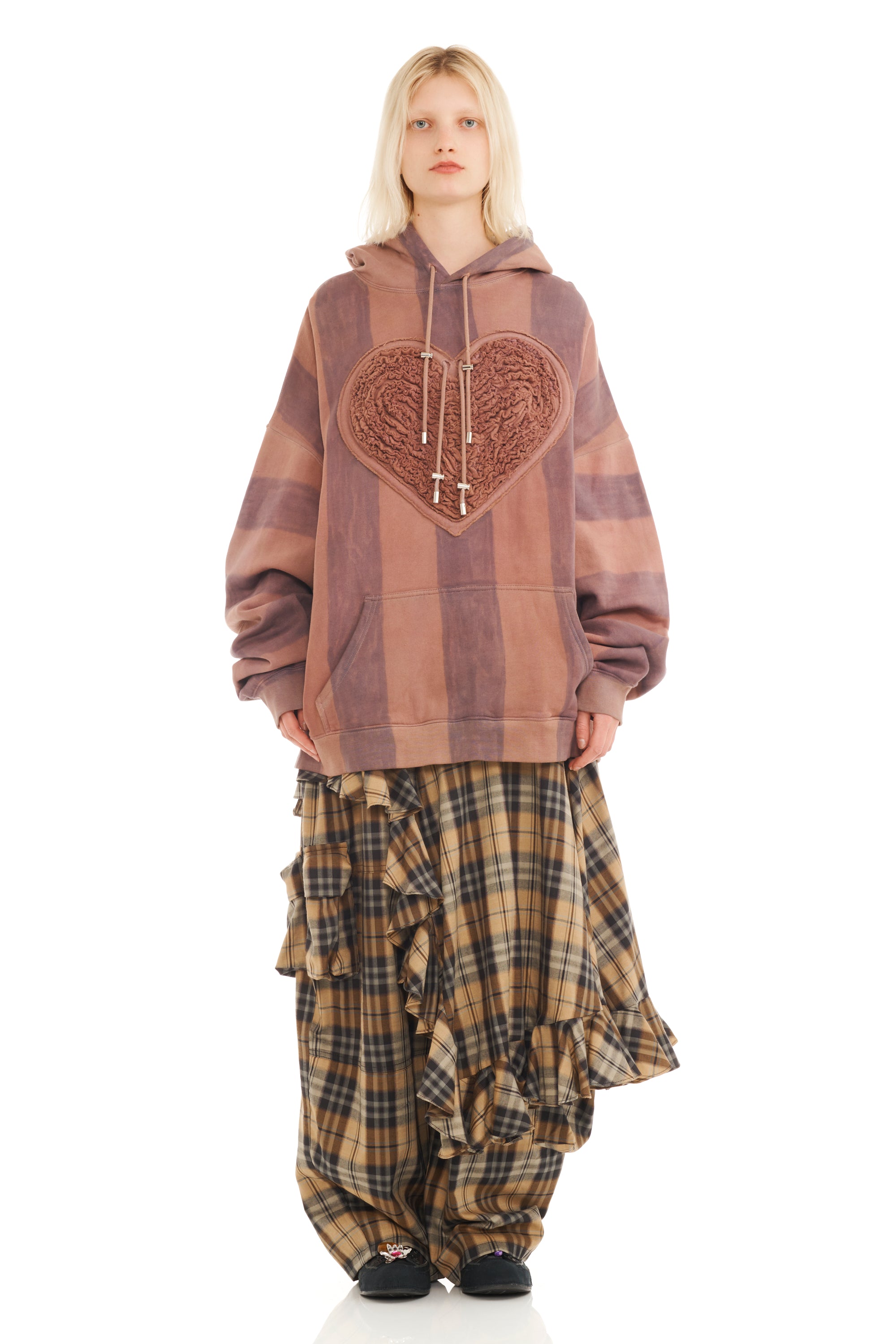 Person wearing a brown striped hoodie with a heart design and plaid pants on a white background