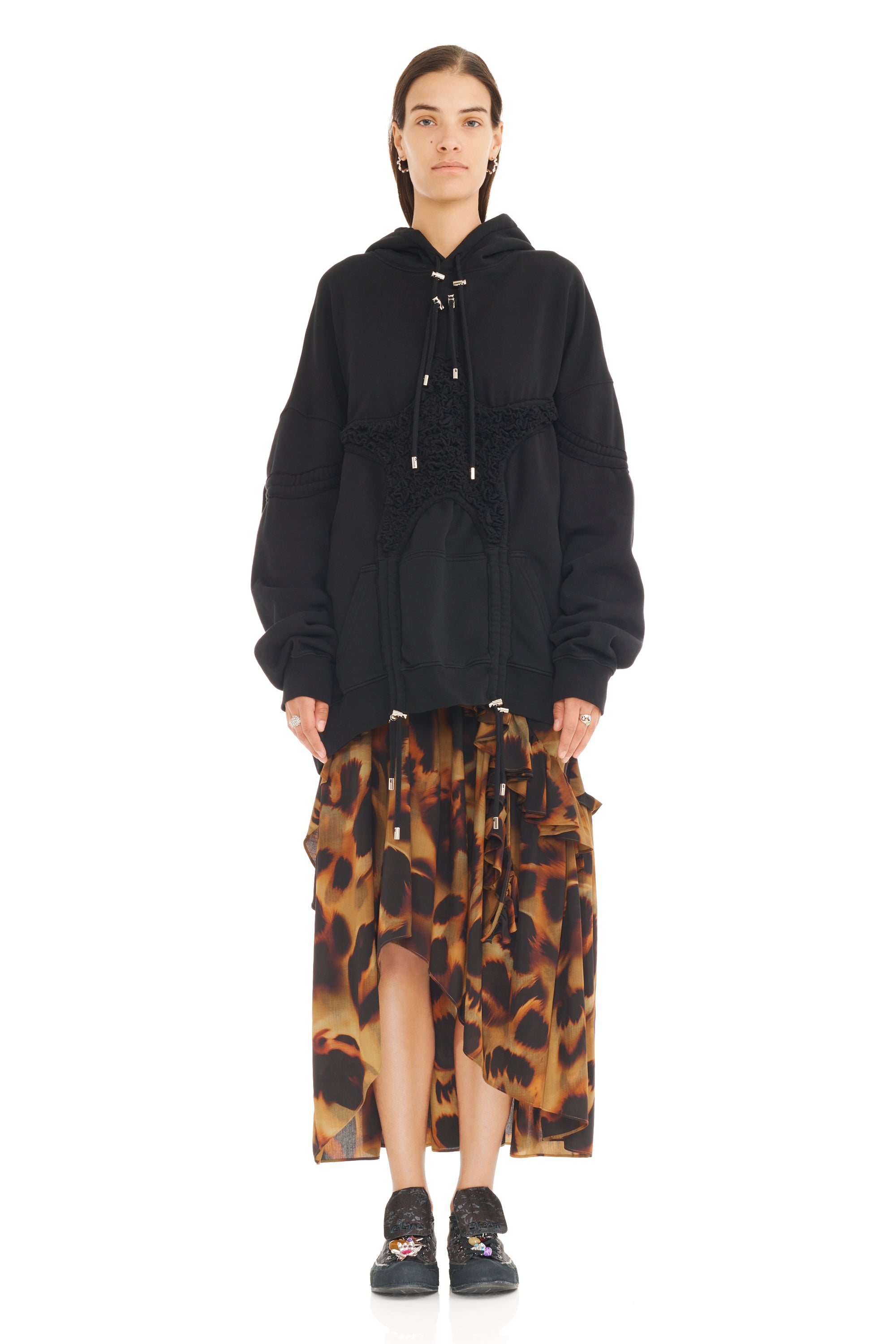 Person wearing a black hoodie and leopard print skirt on a white background