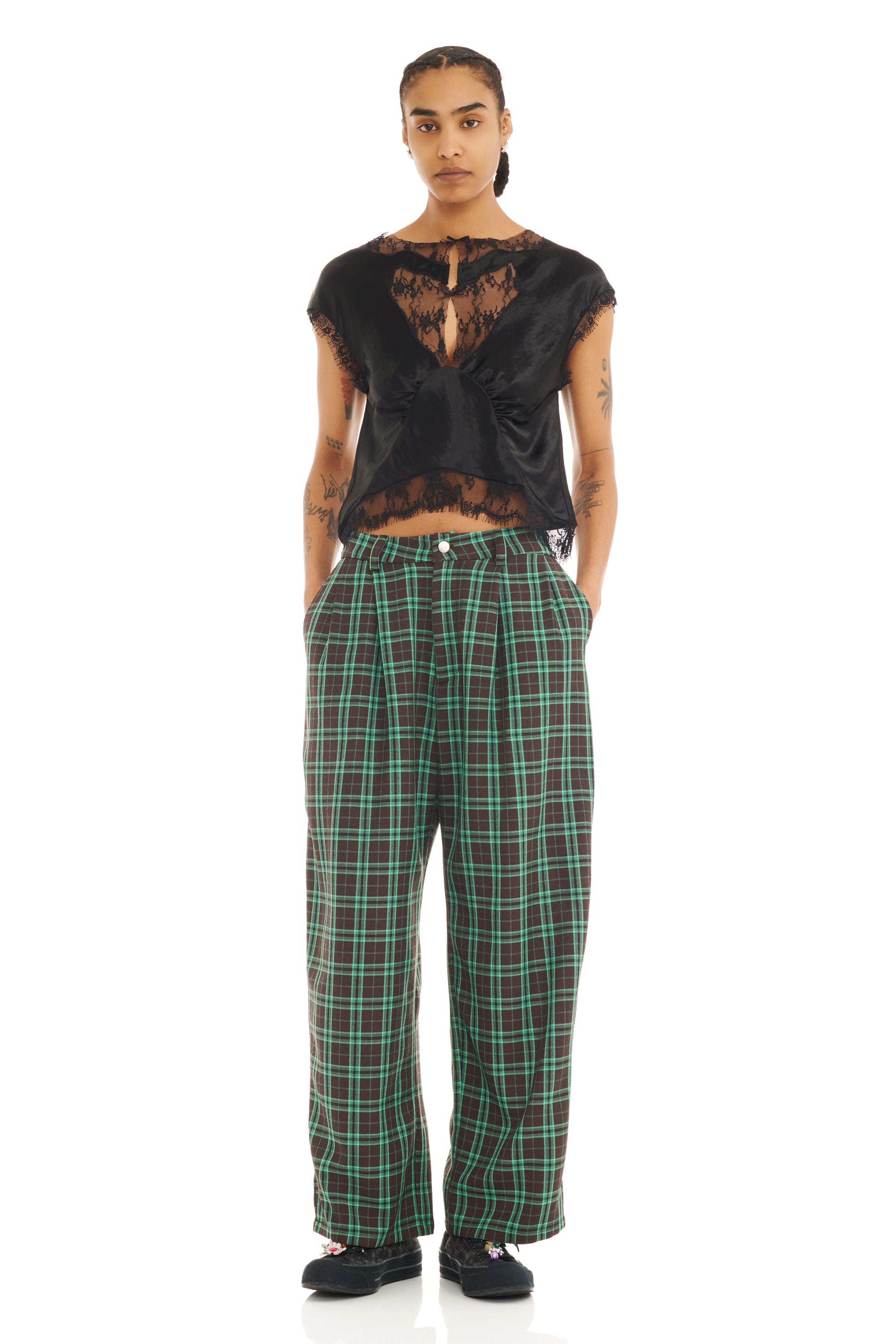 Person wearing a black top with lace details and green plaid baggy pants on a white background